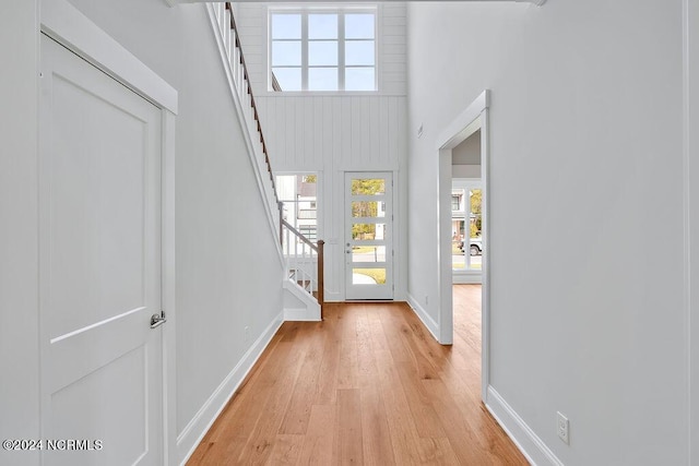 entryway with light wood-type flooring, a towering ceiling, and plenty of natural light