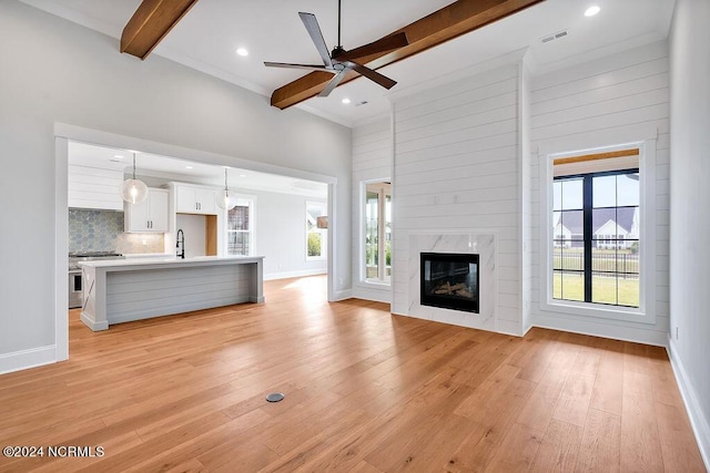 unfurnished living room featuring a high end fireplace, beamed ceiling, light hardwood / wood-style floors, sink, and ceiling fan