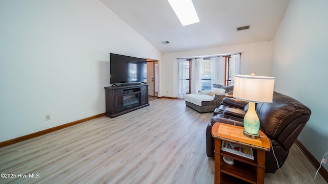 living room with high vaulted ceiling, a skylight, and light hardwood / wood-style floors