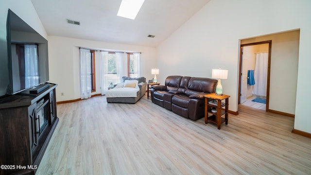 living room with light hardwood / wood-style flooring, high vaulted ceiling, and a skylight