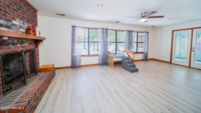 living area with ceiling fan, a brick fireplace, and light wood-type flooring