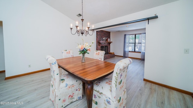 dining room featuring light hardwood / wood-style floors, a brick fireplace, and a notable chandelier