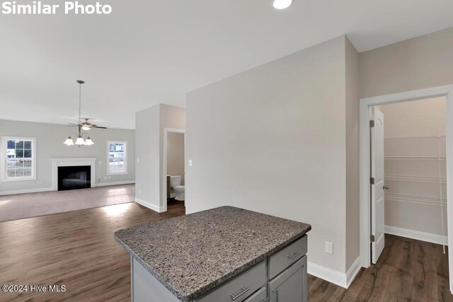 kitchen with ceiling fan, dark hardwood / wood-style floors, a center island, and light stone countertops