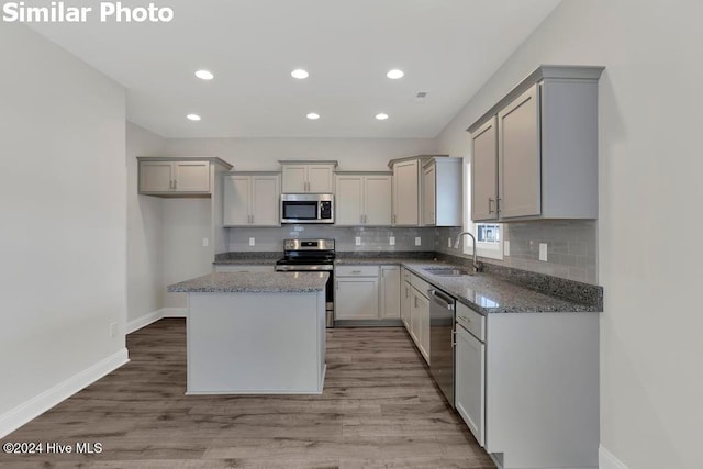 kitchen featuring sink, stainless steel appliances, a center island, dark stone counters, and light wood-type flooring