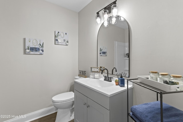 half bath with baseboards, vanity, toilet, and wood finished floors