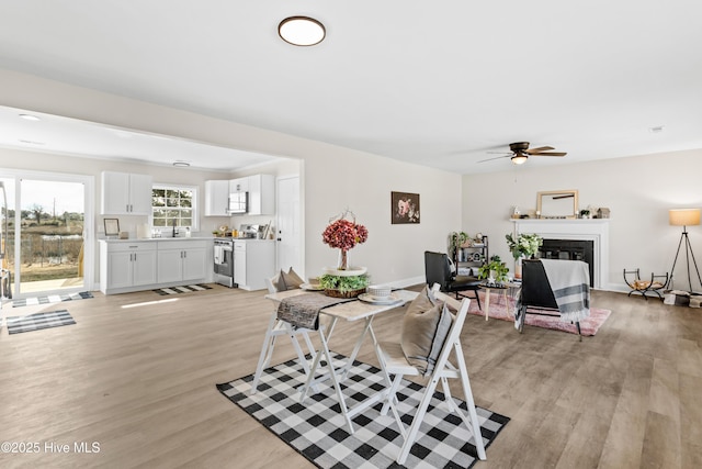 dining area featuring a ceiling fan, a glass covered fireplace, light wood-style flooring, and baseboards