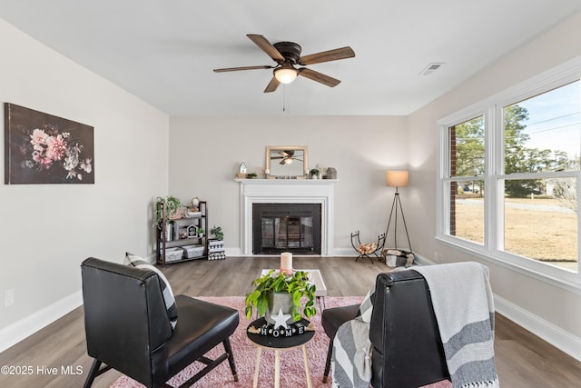 living room featuring wood finished floors, a glass covered fireplace, visible vents, and baseboards