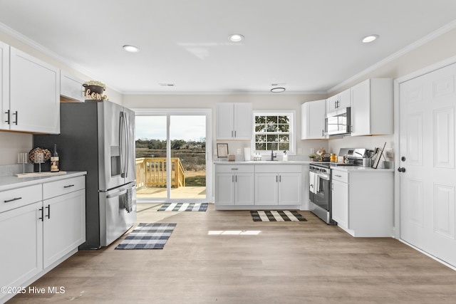 kitchen featuring appliances with stainless steel finishes, light wood-style floors, white cabinetry, and ornamental molding