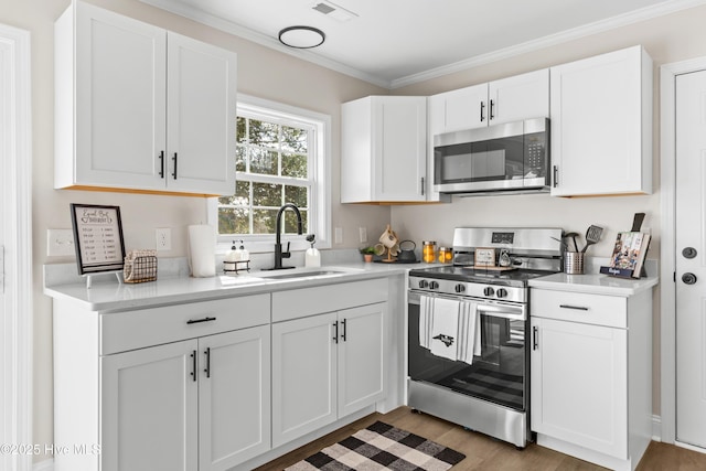 kitchen featuring stainless steel appliances, a sink, white cabinets, light countertops, and crown molding