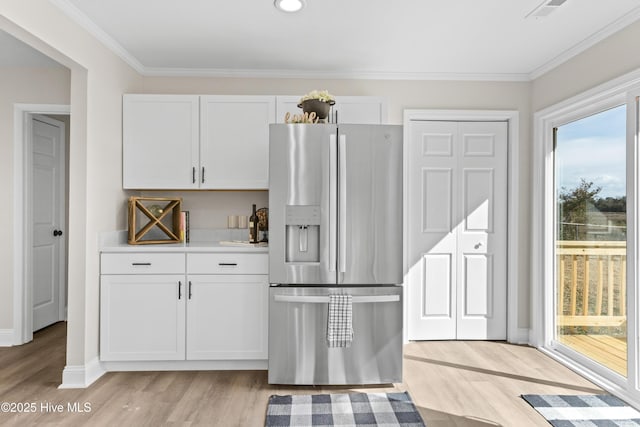 kitchen featuring visible vents, light wood-style flooring, ornamental molding, white cabinetry, and stainless steel fridge