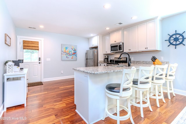 kitchen featuring appliances with stainless steel finishes, white cabinets, a kitchen bar, and light hardwood / wood-style flooring