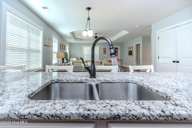 room details with a tray ceiling, light stone countertops, sink, and hanging light fixtures