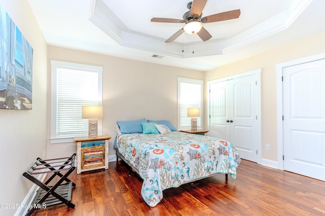 bedroom featuring multiple windows, dark wood-type flooring, ceiling fan, and a tray ceiling