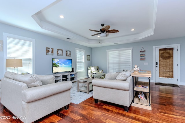 living room featuring dark wood-type flooring, ceiling fan, and a tray ceiling