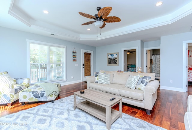 living room featuring dark wood-type flooring, ceiling fan, ornamental molding, and a raised ceiling