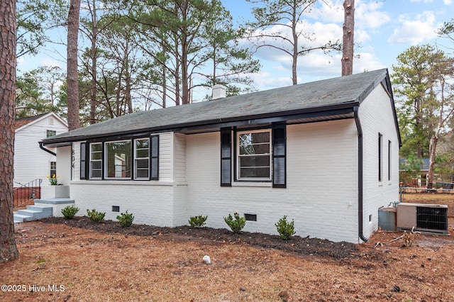 view of front facade with a shingled roof, a chimney, crawl space, cooling unit, and brick siding