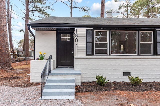 property entrance featuring crawl space, brick siding, a chimney, and roof with shingles