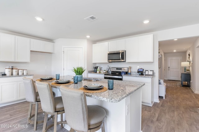 kitchen with light stone countertops, appliances with stainless steel finishes, white cabinetry, and a center island with sink