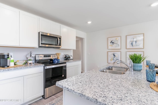 kitchen featuring light hardwood / wood-style floors, light stone countertops, white cabinetry, and stainless steel appliances