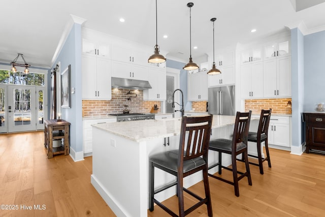 kitchen with white cabinetry, high quality fridge, and a kitchen island with sink