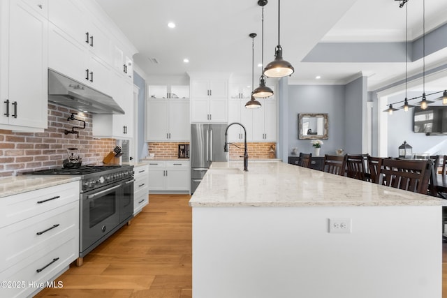 kitchen with high quality appliances, an island with sink, decorative backsplash, and white cabinets