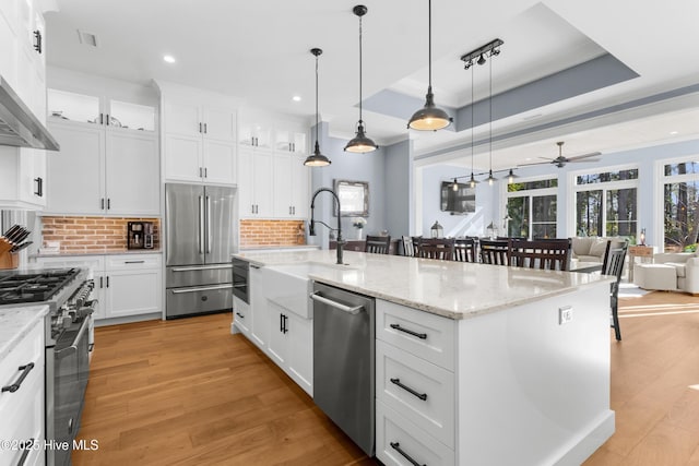 kitchen with decorative light fixtures, stainless steel appliances, a kitchen island with sink, decorative backsplash, and white cabinets