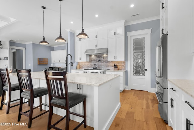 kitchen featuring decorative light fixtures, white cabinetry, a kitchen breakfast bar, light stone countertops, and a center island with sink