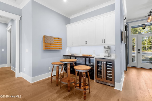 bar with wine cooler, white cabinetry, ornamental molding, and light wood-type flooring