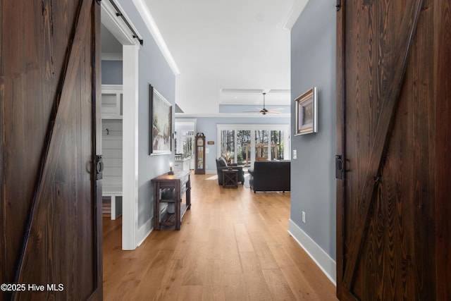 corridor featuring crown molding, light hardwood / wood-style flooring, a barn door, and a raised ceiling