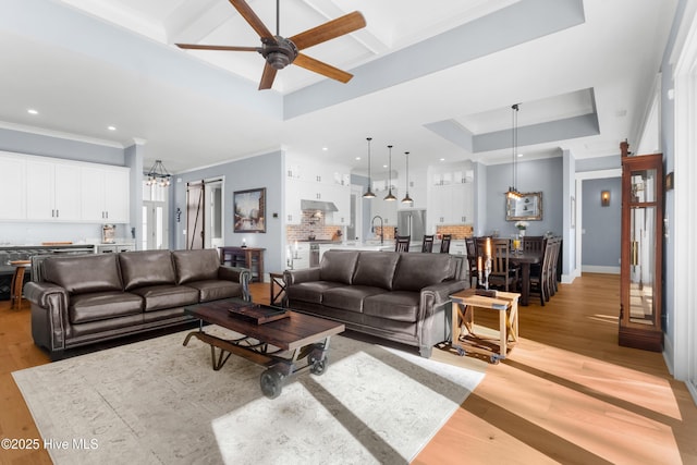 living room with sink, crown molding, ceiling fan, light hardwood / wood-style floors, and a raised ceiling