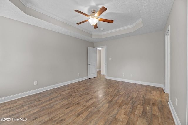 empty room with a textured ceiling, ornamental molding, dark hardwood / wood-style flooring, a raised ceiling, and ceiling fan