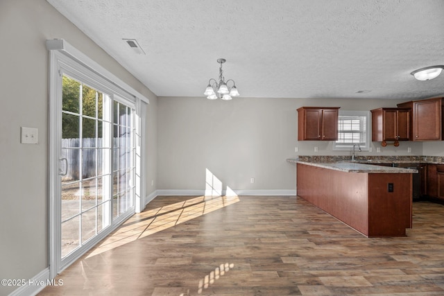 kitchen with an inviting chandelier, hardwood / wood-style floors, hanging light fixtures, a kitchen breakfast bar, and kitchen peninsula