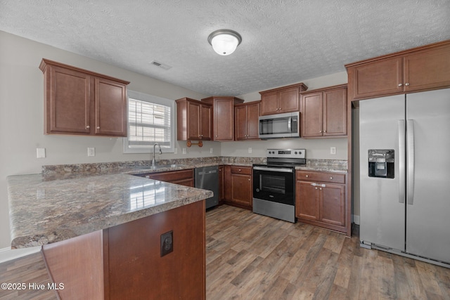 kitchen featuring sink, appliances with stainless steel finishes, light hardwood / wood-style floors, a textured ceiling, and kitchen peninsula