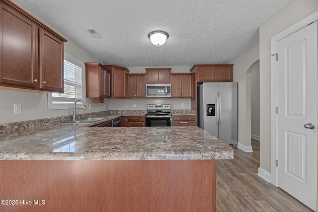 kitchen with sink, dark wood-type flooring, stainless steel appliances, a textured ceiling, and kitchen peninsula