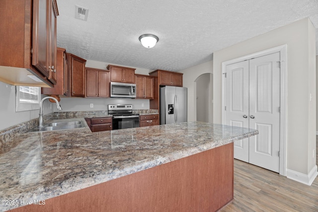 kitchen featuring sink, appliances with stainless steel finishes, light stone counters, light hardwood / wood-style floors, and kitchen peninsula