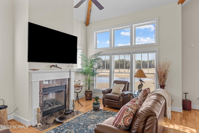 living room with beamed ceiling, wood-type flooring, high vaulted ceiling, a premium fireplace, and ceiling fan