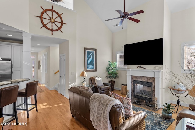 living room with a premium fireplace, light wood-type flooring, high vaulted ceiling, and ceiling fan