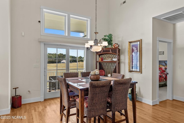 dining room featuring light wood-type flooring, a towering ceiling, and an inviting chandelier