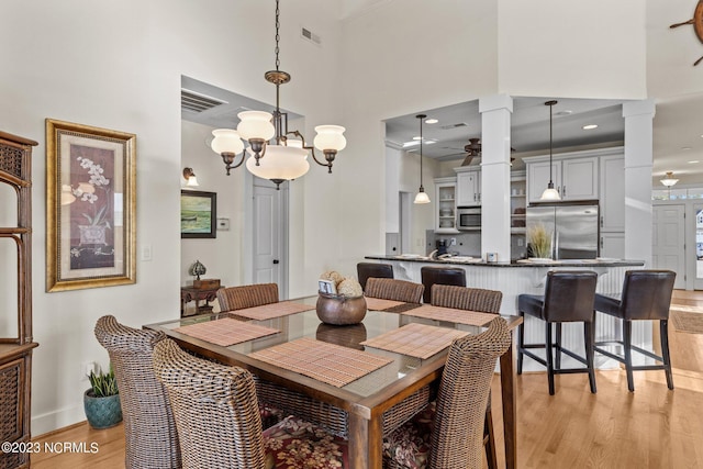 dining room featuring ceiling fan with notable chandelier, light hardwood / wood-style flooring, a towering ceiling, and ornate columns