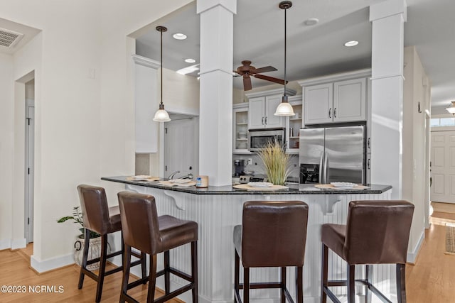 kitchen featuring appliances with stainless steel finishes, decorative light fixtures, light hardwood / wood-style floors, kitchen peninsula, and decorative columns