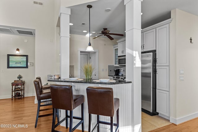 kitchen featuring kitchen peninsula, hanging light fixtures, appliances with stainless steel finishes, and ornate columns