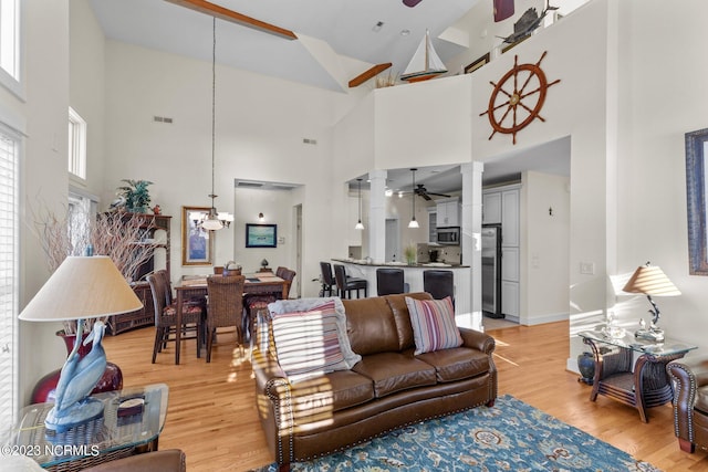 living room featuring decorative columns, light wood-type flooring, high vaulted ceiling, and ceiling fan