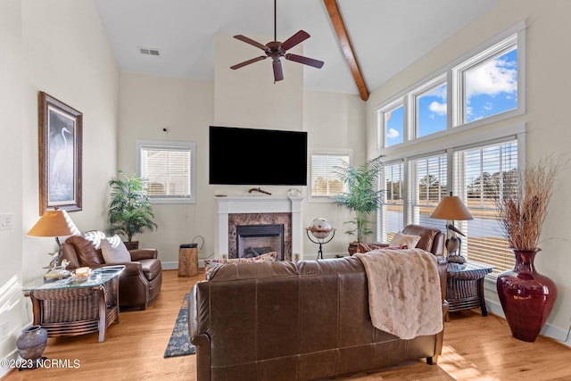 living room featuring a premium fireplace, beamed ceiling, ceiling fan, high vaulted ceiling, and light hardwood / wood-style flooring