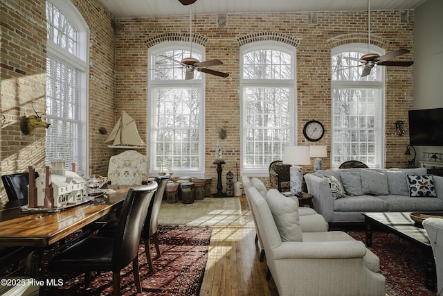 interior space with ceiling fan, brick wall, a healthy amount of sunlight, and hardwood / wood-style flooring