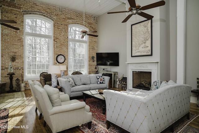 living room with a fireplace, a towering ceiling, dark wood-type flooring, plenty of natural light, and brick wall