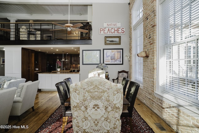 dining area featuring brick wall, dark hardwood / wood-style flooring, plenty of natural light, and a towering ceiling