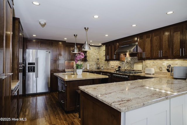 kitchen featuring backsplash, wall chimney range hood, a center island, stainless steel fridge, and light stone counters