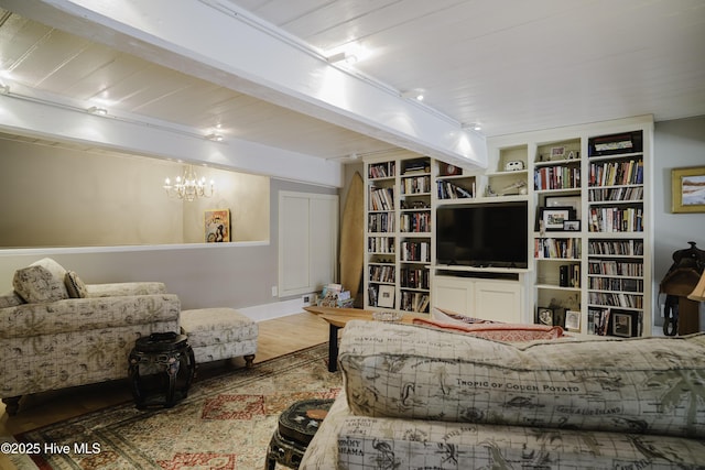 living room featuring an inviting chandelier, rail lighting, hardwood / wood-style flooring, beam ceiling, and built in shelves