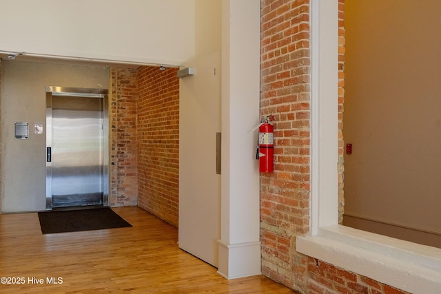 interior space featuring brick wall, light hardwood / wood-style floors, and elevator