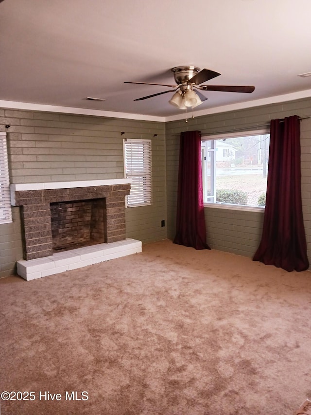 unfurnished living room with ceiling fan, brick wall, carpet flooring, and a fireplace